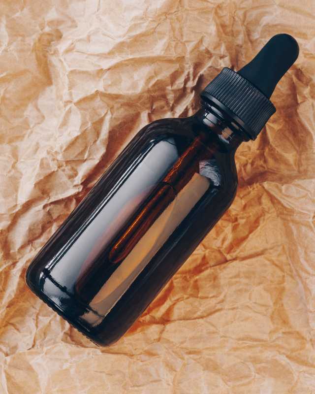 Dark amber RSO tincture bottle with dropper on textured background